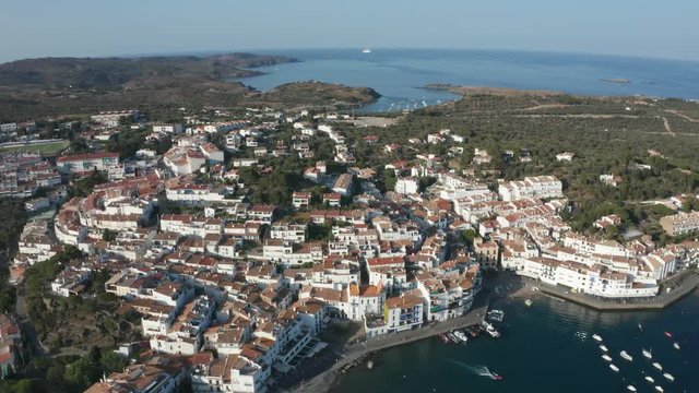 Aerial view of tiled roofs, narrow streets, white houses of resort coastal town Cadaques on Cap de Creus peninsula. Drone shot of boats and yachts anchored in bay on background of scenic cityscape