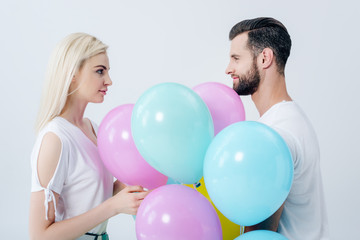 Fototapeta na wymiar man and beautiful girl with balloons looking at each other isolated on grey
