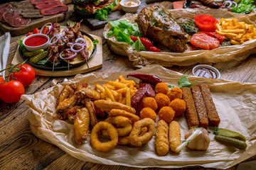 Still life, assorted beer snacks, kebabs skewers, black burger with meat, meat slices on wooden table