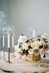 Flowers in golden vase with extinguished candles in vintage brass candle holders on the table