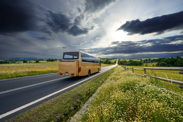 Bus traveling on the asphalt road in rural landscape at sunset with dramatic clouds