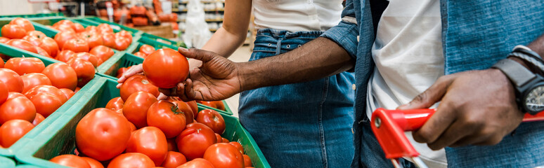 panoramic shot of african american man holding fresh tomato near girl in supermarket