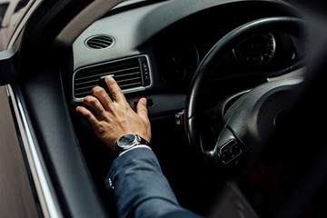cropped view of african american businessman in suit touching air conditioning near steering wheel...