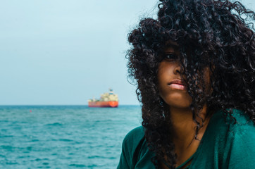 Young girl with black hair, laughing hair sitting on her back to the Caribbean Sea, enjoying a summer day with the wind in her hair, lifestyle portrait - obrazy, fototapety, plakaty