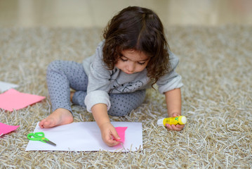 Cute little girl make applique, glues pink , applying a color paper using glue stick while doing...