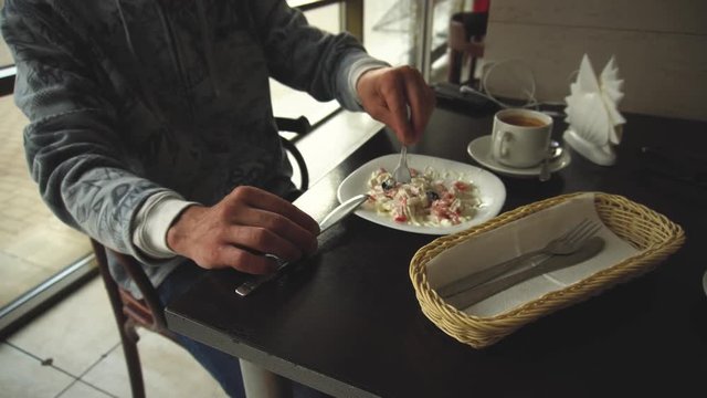 Cropped image of a man during a lunch break who eats a salad while sitting at a wooden table and the waiter brings a pancake