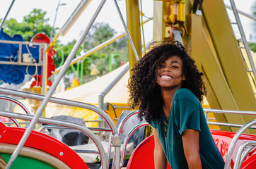 young girl of black color, laughing hair in ferris wheel, sitting enjoying a summer day, lifestyle portrait