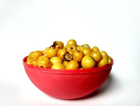Yellow nances Central American fruit in a red bowl with white background