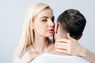 beautiful girl looking at camera and embracing man isolated on grey