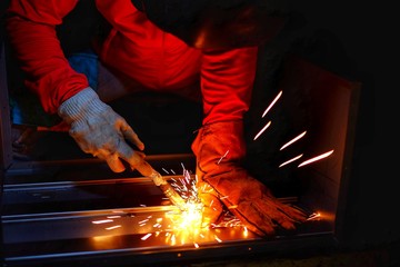 A woman wearing a pink long sleeve jacket, welding mask and leather gloves, welding a metal case...