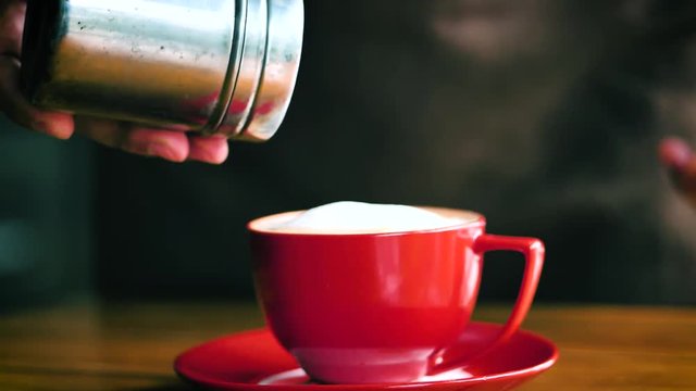 Hand sprinkles chocolate powder on red coffee mug.