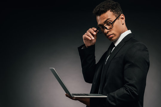 african american businessman holding laptop and looking at camera on dark background