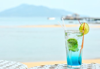 Cold refreshment drinks with blurry beach scenery background. Blue lagoon cocktail on the beach