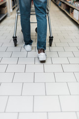 cropped view of man in blue jeans walking with shopping cart