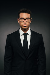 african american businessman in glasses and suit on dark background