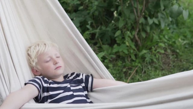 Happy boy blond sleeps in hammock in summer at the cottage
