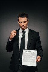 thoughtful african american businessman showing contract on dark background