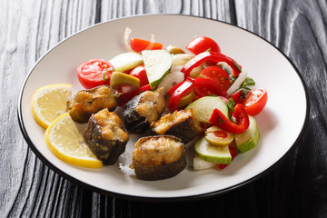 Slices of fried eel fish with fresh vegetable salad and lemon close-up on a plate. horizontal