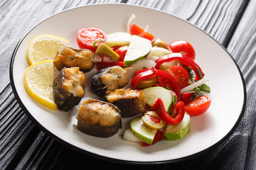 Delicious fish fried European eel with fresh vegetable salad and lemon closeup on a plate. horizontal