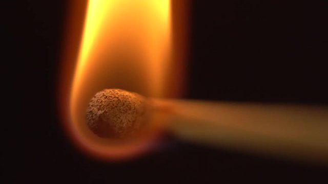 Close up macro shot of set fire to a green head match in slow motion on a black background.
