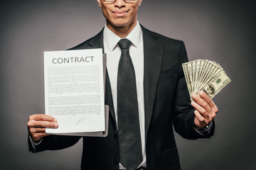 cropped view of happy african american businessman showing contract and holding cash on dark background