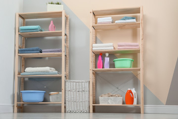 Wooden shelving units with clean towels and detergents in stylish room interior