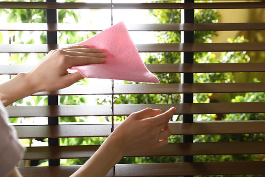 Woman wiping window blinds with rag indoors, closeup