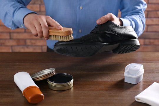 Man cleaning leather shoe at wooden table indoors, closeup
