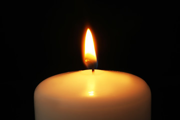 Burning candle on dark background, closeup. Symbol of sorrow