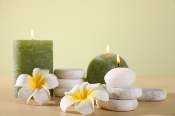 Fototapeta na wymiar Composition of spa stones, flowers and burning candles on wooden table against light green background