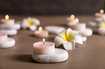 Fototapeta na wymiar Composition of spa stones, flowers and burning candles on wooden table