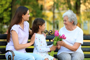 Grandmother receiving bouquet of flowers from her family on bench in park