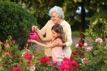 Little girl and her grandmother watering flowers in garden