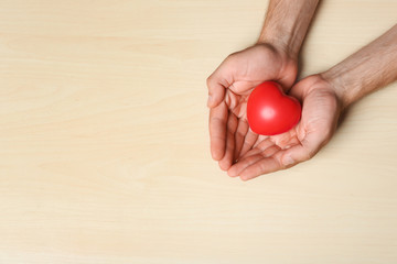 Young man holding red heart on light wooden background, top view with space for text. Donation concept