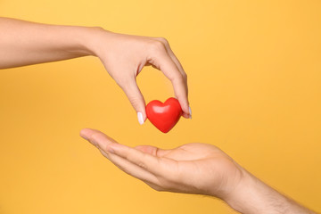 Woman giving red heart to man on yellow background, closeup. Donation concept