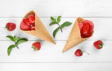 Delicious strawberry ice cream in wafer cones on white wooden table, flat lay