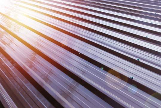 Corrugated metal roofing in brown paint color..Rust resistance corrugated aluminium roofing with surface reflection of sunlight ,shade of palm tree and lens flare.