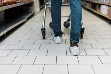 cropped view of african american man in blue denim jeans walking with shopping cart