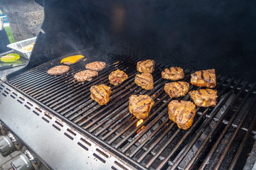 Propane outdoor gas grill on a deck with hamburgers and pork chops
