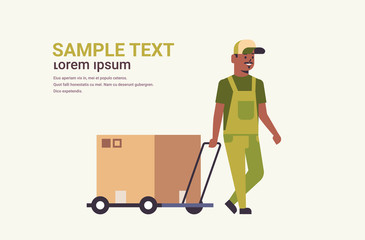courier in uniform pushing trolley with cardboard box package mail express delivery service concept african american worker with hand truck flat full length horizontal copy space