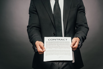 cropped view of african american businessman showing contract on dark background