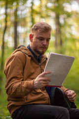 One man reading notebook papers, in forest.