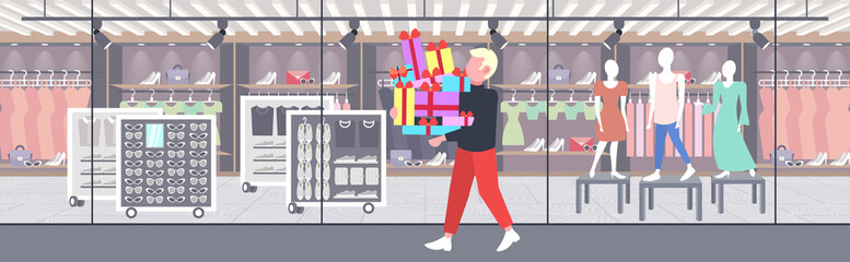 man carrying stack of wrapped gift boxes big seasonal sale shopping concept guy holding colorful presents modern boutique fashion shop exterior flat full length horizontal
