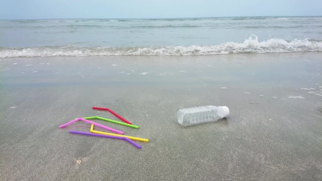 Colorful plastic straws bottle single use on the sand in the ocean with ocean waves. The people throwing trash carelessly in anywhere not a bin. Environment negligently concept.