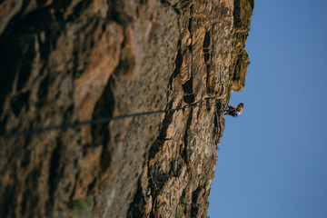 Silhouette of a woman climbing on cliff against brown cracked rock and blue sky