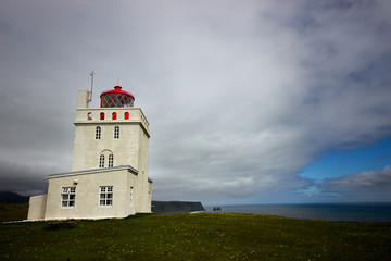Fototapeta na wymiar The lighthouse of Dyrholaey stands lonely above the cliffs and trolls fingers at the south coast of Iceland not far from the village of Vik. Cloudy dramatic sky