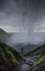 Silhouette of a man standing under the huge waterfall. Visible Streams of water. Dramatic cloudy sky. Iceland