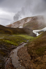 Small river flowing through the geyser valley in Iceland. Beautiful landscape with steam column and dramatic sky background. Landmannalaugar, Iceland