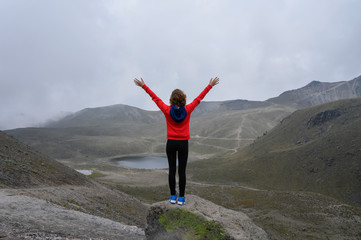Long Shot of a girl reaching the top of a mountain, raising her arms and watching the landscape