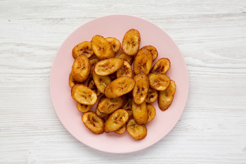 Homemade fried plantains on a pink plate over white wooden background, top view. Flat lay, overhead, from above. Close-up.